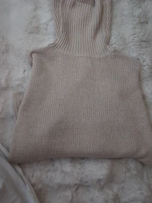 Beige stickad polokrage - Säljer en beige stickad polokrage i mjukt material. Perfekt att bära över en tröja eller jacka för extra värme. Polokragen har ribbstickade detaljer och en enkel, stilren design som passar till det mesta.