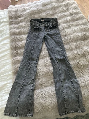 Grå bootcut jeans från Nelly - Säljer ett par grå bootcut jeans från Nelly med markerade sömmar och dubbla knappar i midjan. Jeansen har unika fyrkantiga fickor framtill och är tillverkade i denim med tvättad look. Perfekta för dig som vill ha en cool och trendig stil.