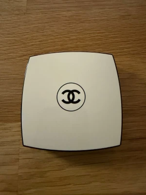 Chanel le beige pounders healthy glow sheer  - Lyxig poudre från Chanel i en elegant vit kompakt dosa med spegel och tillhörande borste. Dosan har den ikoniska Chanel-loggan på locket och borsten är mjuk och halvmåneformad för enkel applicering. Perfekt för att skapa en solkysst look.