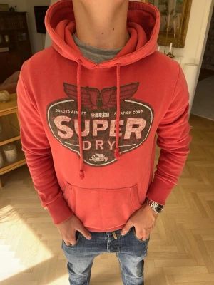 Superdry hoodie röd herr  - 🔥 Superdry hoodie i snygg röd färg! Perfekt till vardag, skola eller streetwear. Mjuk, bekväm och lätt att matcha med jeans eller cargos. Fint använt skick.  📏 Storlek: S 📦 Snabb frakt & paketrabatt vid köp av flera plagg!  Sökord: Superdry hoodie, huvtröja, sweatshirt, streetwear, vintage, casual, premium, herr, unisex, hoodie S, röd hoodie, höst, vinter, Y2K, college