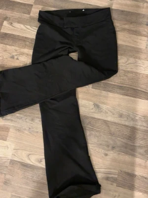 Svarta bootcut kostymbyxor  - Säljer ett par svarta kostymbyxor med bootcut-modell och bred linning. De är stretchiga och sitter skönt på kroppen, perfekta till en avslappnad look. Materialet känns mjukt och följsamt. Passar dig som gillar enkel och stilren design.