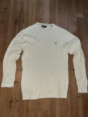 Vit kabelstickad tröja från Gant - Kabelstickad vit tröja från Gant med rund halsringning och diskret logga broderad på bröstet. Tröjan har långa ärmar och ribbade muddar vid ärmslut och nederkant. Perfekt för dig som gillar klassisk och stilren design. Aldrig använd utan köpt och varit för stor! Nyskick!     Nypris:1599kr.       Mitt pris:849