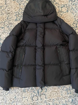 Syna world  - Helt ny inte använd äkta syna world puffer jacka som är helt svart med svart logga på luvan med jätte många små detaljer kom Järna privat om du vill ha mer bilder 