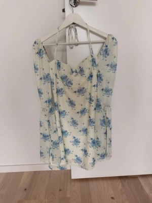 Vit kortklänning med blå blommor -  Jättefin vit klänning från Cider med blått blommönster🦋. Figurnära modell med markerade kupor, knytning i nacken och långa utsvängda ärmar i mesh. ”Fodrad” i själva klänningen. Endast använd en gång och i väldigt fint skick🩵. Storlek S.