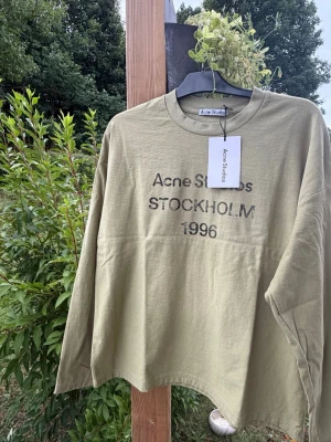 Beige långärmad t-shirt Acne Studios - Snygg grön långärmad t-shirt från Acne Studios med tryck 'STOCKHOLM 1996' på bröstet. Tillverkad i mjuk bomull och har en relaxed, loose passform. Perfekt för dig som gillar stilrena plagg med en urban touch.