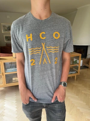 Hollister vintage T-shirt grå med tryck herr - Hollister T-shirt i mörkgrått med orange/gul HCO-tryck. Storlek M. Clean och avslappnad design som passar till det mesta. Bra skick.  #Hollister #HCO #Tshirt #Herrkläder #Casual #Streetwear #Preppy #SizeM #M