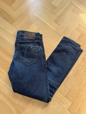 Mörkblå slim fit jeans - Mörkblå G star raw jeans med hårt denim tyg. Börjar få snygga fades men har tyvärr blivit för korta för mig. Sitter väldigt bra och kommer fortsätta fadeas när du använder dom! 31/34, 