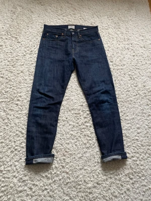 Cof studio selvedge jeans  - Säljer ett par mörkblå selvedge jeans med klassisk femficksmodell och upprullade benslut. Jeansen har raka ben och tydliga kontrastsömmar. Materialet är kraftig denim i 100% bomull, perfekt för dig som gillar tidlös och clean stil.