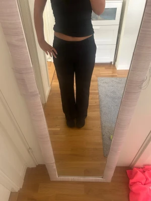 Svarta raka kostymbyxor - Säljer ett par svarta kostymbyxor med utsvängda ben och normal midja. Byxorna har diskreta fickor på sidorna och är perfekta för en clean och stilren look. Materialet ser ut att vara mjukt och följsamt, vilket gör dem bekväma att bära hela dagen.