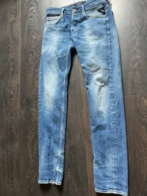Blå slim fit jeans med slitningar - Snygga blå slim fit jeans med slitna detaljer och ljusa partier på låren och knäna. Klassisk femficksmodell med dragkedja och knapp i midjan. Bakfickorna har dekorativa sömmar. Perfekta för en avslappnad och trendig look.