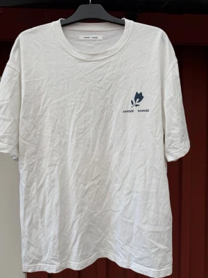 Vit t-shirt från Samsøe Samsøe - Vit t-shirt från Samsøe Samsøe med blått tryck fram och stort grafiskt tryck på ryggen. Rund halsringning och avslappnad passform. Perfekt för en chill och stilren look.