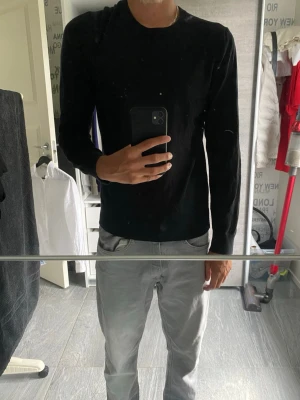 Svart långärmad tröja i bomull - En enkel och stilren svart långärmad tröja med rund halsringning. Tröjan har en smal passform och är tillverkad i ett mjukt bomullstyg som passar perfekt till jeans eller chinos. Perfekt basplagg för garderoben. 