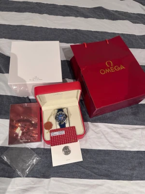 Omega Seamaster blå klocka - Säljer en Omega Seamaster klocka med blått och silverfärgat boett. Urtavlan har världskarta och flera tidszoner, samt detaljer i blått och silver. Kommer med originalbox, certifikat och Omega-påse. Perfekt för dig som gillar exklusiva accessoarer.❗️PRIS KAN DISKUTERAS❗️