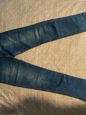 Mörkblå slim fit jeans - Säljer ett par mörkblå slim fit jeans med lätt slitningar och klassiska fem fickor. Jeansen har en snygg tvätt och kontrastsömmar. Perfekta för dig som gillar en smalare passform och tidlös stil.