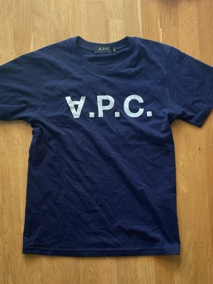  A.P.C. t-shirt - Tja! Jag säljer en Snygg marinblå t-shirt från A.P.C. med stort vitt logotryck på bröstet. Klassisk rund hals och korta ärmar. Tillverkad i mjuk bomull som känns skön mot huden. Perfekt för en clean och stilren look.