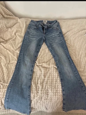 Ljusblå bootcut jeans från BDG - Säljer ett par ljusblå bootcut jeans från BDG med klassisk femficksdesign och dragkedjegylf. Jeansen har snygga slitningar och en lätt tvättad look. Perfekta för dig som gillar retrovibbar och vill ha ett par jeans med lite vidare ben.