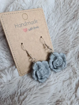 Handgjorda glittriga rosörhängen - Unika handgjorda örhängen i form av rosor, tillverkade i glittrande silverfärgad lera. Örhängena har silverpläterade krokar och är gjorda för hand av mig i polymerlera. 
