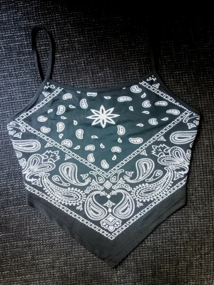 Bandana linne  - svart topp med vitt bandanamönster och smala axelband. Toppen har en spetsig nederkant och är perfekt för en cool och avslappnad stil. Materialet är mycket strechigt.
