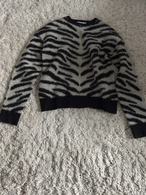 Zebramönstrad stickad tröja NA-KD - Säljer en stickad tröja från NA-KD i storlek S med zebramönster i svart och grått. Tröjan har rund halsringning, långa ärmar och ribbade muddar vid ärmslut och nederkant. 