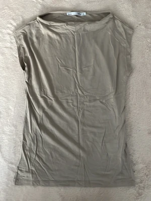 Beige ärmlös topp med rak hals - En stilren beige topp med rak halsringning och ärmlös design. Toppen har en enkel och clean look, perfekt att matcha med olika outfits. Tillverkad i ett mjukt och lätt material som känns skönt mot huden. 