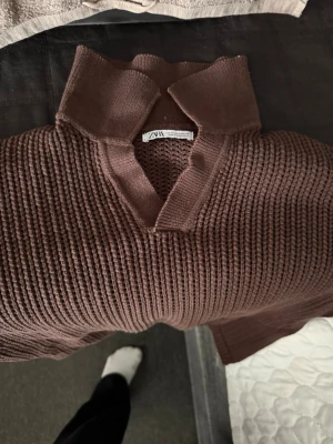 Brun stickad tröja från Zara - Mysig brun stickad tröja från Zara med krage och v-ringad öppning. Tröjan har grovstickad struktur och långa ärmar. Perfekt för lager på lager och ger en avslappnad men ändå stilren look.
