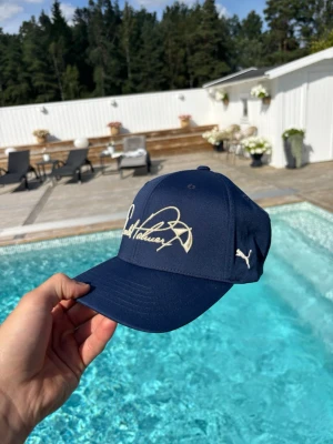 Mörkblå Golfkeps från Puma - Snygg mörkblå Golfkeps från Puma med vit broderad logga på sidan och cool signaturdesign framtill. Klassisk böjd skärm och justerbar baksida. Perfekt accessoar för en sportig och avslappnad stil. Köpt för 400kr i butik och är helt ny. Använd Max 5 gånger.