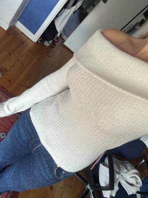 Off shoulder vit stickad tröja - Säljer en snygg off shoulder stickad tröja i vit färg. Tröjan har ribbad struktur, långa ärmar och en bred krage som sitter snyggt över axlarna. Perfekt för dig som vill ha en trendig och bekväm look till hösten eller vintern.