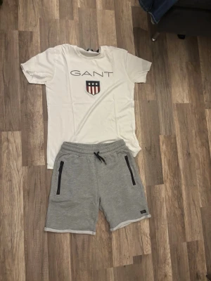 Grå mjukisshorts med snörning - Snygga grå mjukisshorts med svarta dragkedjor på fickorna och snörning i midjan. Perfekta för chill dagar eller träning. Shortsen har en relaxed fit och är gjorda i mjukt bomullsmaterial. Med en vit gant tröja med storlek S