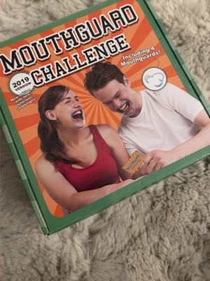 Mouthguard Challenge sällskapsspel - Mouthguard Challenge är ett partyspel där du använder munöppnare och försöker prata, gissa och utföra utmaningar. Spelet innehåller 4 munöppnare och 55 kort med olika utmaningar. Perfekt för skrattfyllda spelkvällar med vänner! För 2-6 spelare, från 12 år.