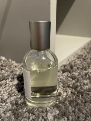 Northrop 25.0 extrait de parfum - En stilren parfymflaska med transparent glas och silvrig kork. Etiketten är vit med svart och röd text där det står 'Northrop 25.0 extrait de parfum' och 'one bold chemist'. Flaskan har en rund form och innehållet är klart.Parfymen luktar mer åt citron hållet.