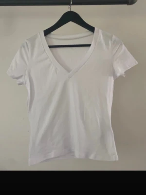 Vit v-ringad t-shirt - Klassisk vit t-shirt med v-ringning och korta ärmar. Enkel och stilren modell i mjukt bomullstyg som passar perfekt till jeans eller shorts. Snygg passform och ett måste i garderoben för en clean look.