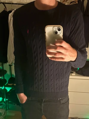 Mörkblå kabelstickad tröja Polo Ralph Lauren - Snygg mörkblå kabelstickad tröja från Polo Ralph Lauren med klassisk röd logga på bröstet. 