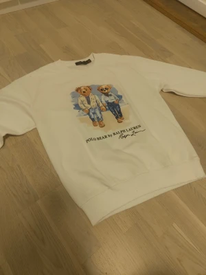 Vit sweatshirt Polo Bear Ralph Lauren - Vit sweatshirt från Ralph Lauren med Polo Bear-tryck framtill. Tröjan har rund halsringning och långa ärmar. Säljer pga ingen användning.