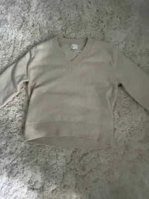 Beige tröja med v-ringning - En stilren beige  tröja med v-ringad hals och långa ärmar. Tröjan har ribbade muddar vid ärmslut och nederkant, vilket ger en snygg och bekväm passform. Perfekt att matcha med jeans eller kjol för en enkel och trendig look.🥰 pris kan discuteras