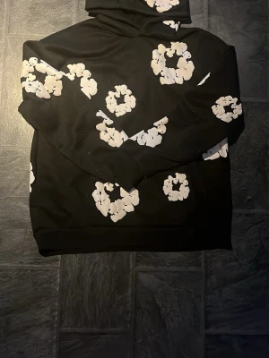 Svart denim tears hoodie - Cool svart hoodie från denim tears Hoodien har en klassisk huva och en avslappnad passform. Perfekt för dig som vill sticka ut med en unik och trendig stil.
