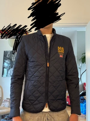 Marinblå quiltad höst jacka från Morris - Snygg marinblå quiltad jacka från Morris med guldfärgad logga och brittisk flagga på bröstet. Jackan har dragkedja framtill, ståkrage och lång ärm. Perfekt för dig som vill ha en stilren och klassisk look. Perfekt till hösten/skolstarten. Inga defekter jag kunde se, väldigt omhändertagen. Jag bär M och den sitter för litet på mig. Den är true to size .