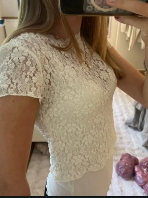 Vit spetsblus med blommönster - Säljer en söt vit blus i spets med blommigt mönster. Toppen har korta ärmar och en något croppad passform. Perfekt för dig som gillar romantisk och feminin stil. Supersnygg att styla med både jeans och kjol!