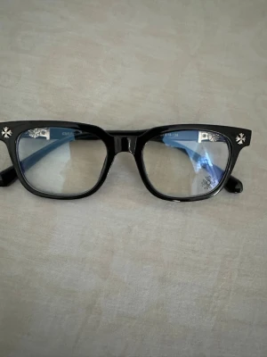 chrome hearts glasögon  - Snygga solglasögon med svart, fyrkantig båge och coola silverfärgade detaljer vid hörnen. Glasen har en lätt toning och bågarna är i plast. Perfekta för dig som vill ha en stilren men ändå unik look.