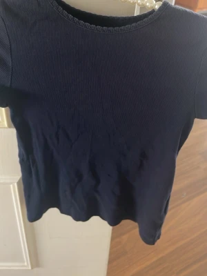 Mörkblå ribbad t-shirt - En enkel och stilren mörkblå t-shirt med ribbad struktur. T-shirten har korta ärmar och rund halsringning. Perfekt basplagg till garderoben och lätt att matcha med olika stilar.