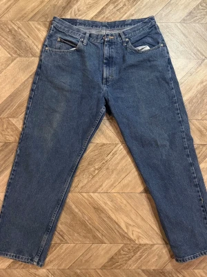 Wrangler Relaxed jeans - Säljer ett par blå jeans med rak passform och fem fickor. Jeansen har hög midja och klassisk dragkedja med knapp. Tillverkade i denim, perfekt för en avslappnad stil. Passar dig som gillar tidlösa och enkla jeans. Längd 98cm Bredd 40cm  