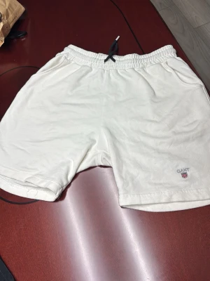 Vita shorts Gant - Snygga vita shorts från Gant i mjuk frotté med elastisk midja och snörning. Shortsen har fickor på sidorna och en liten broderad Gant-logga framtill. Perfekta för sommardagar när du vill vara både bekväm och stilren.