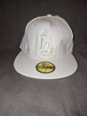 Vit LA 59FIFTY keps - Snygg vit keps från New Era med LA-logga framtill. Klassisk 59FIFTY-modell med rak skärm och broderade detaljer. Kepsen är i bomullsmaterial och har autentiska etiketter kvar både på insidan och utsidan.