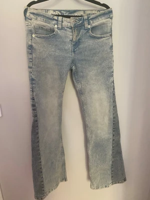 Ljusblå bootcut jeans från H&M  - Säljer ett par ljusblå bootcut jeans från H&M  i storlek 40. Jeansen har klassisk femficksmodell, låg/mid midja och  utsvängda ben. Tillverkade i bomull med en snygg tvättad look och slitningar för en trendig vibe.
