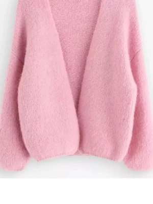 Lindex rosa kofta - Mysig ljusrosa kofta med öppen front och ballongärmar. Koftan är stickad i ett fluffigt material som ger en soft och trendig look. Perfekt att slänga över en t-shirt eller topp för extra värme och stil.