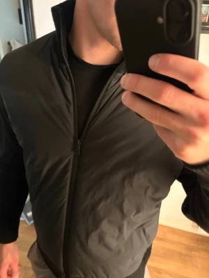 Jacka från J.Lindeberg - Snygg svart bomberjacka med ribbade muddar och stickade ärmar. Jackan har dragkedja framtill och en hög krage. Perfekt för dig som gillar en stilren look med sportig touch.