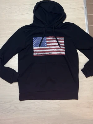Svart hoodie med amerikansk flagga - Säljer en fet usa hoodie! Helt oanvänd. Finns i alla storlekar, pris diskuteras och skickar gärna fler bilder eller mått!😊
