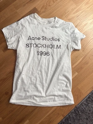 Vit Acne Studios t-shirt Stockholm - Vit t-shirt från Acne Studios med tryck 'STOCKHOLM 1996' på bröstet. Klassisk passform med rund hals och korta ärmar. Perfekt för dig som gillar minimalistisk och stilren design.
