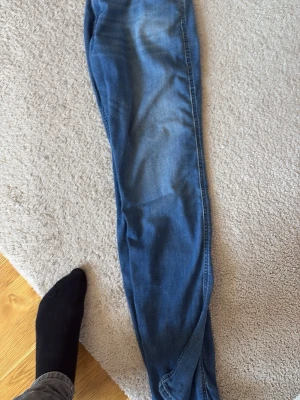 Blå jeans från Replay - Säljer ett par blå jeans från Replay med klassisk modell och smal passform. Jeansen har snygga slitningar och är tillverkade i mjukt denimtyg som ger en skön känsla. Perfekta för dig som gillar en avslappnad men ändå stilren look.
