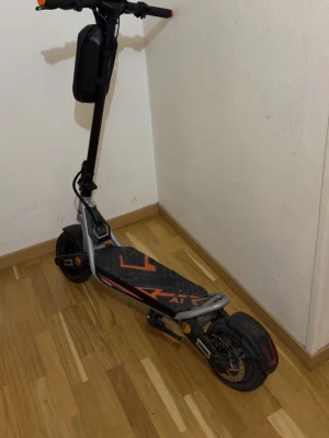 Kukirin a1 - Säljer en elsparkcykel i svart och orange med robust ram och bred fotplatta. Utrustad med stora hjul, skivbroms bak och förvaringsväska på styret. Snygg design med grafiska detaljer på plattan och reflexdetaljer på sidorna. Märket är kukirin a1 kommer utan laddare för frågar Ele information om urfunktionen skriv till mig i dms 