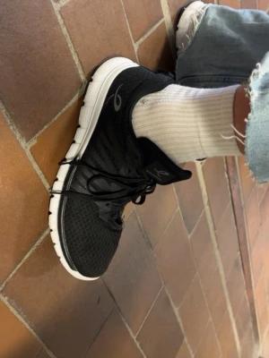 Svarta sneakers med vit sula - Snygga svarta sneakers med vit sula och svart snörning. Ovandelen är i meshmaterial för bra ventilation och komfort. Diskret logga på sidan och tungan. Perfekta för en sportig och avslappnad stil.